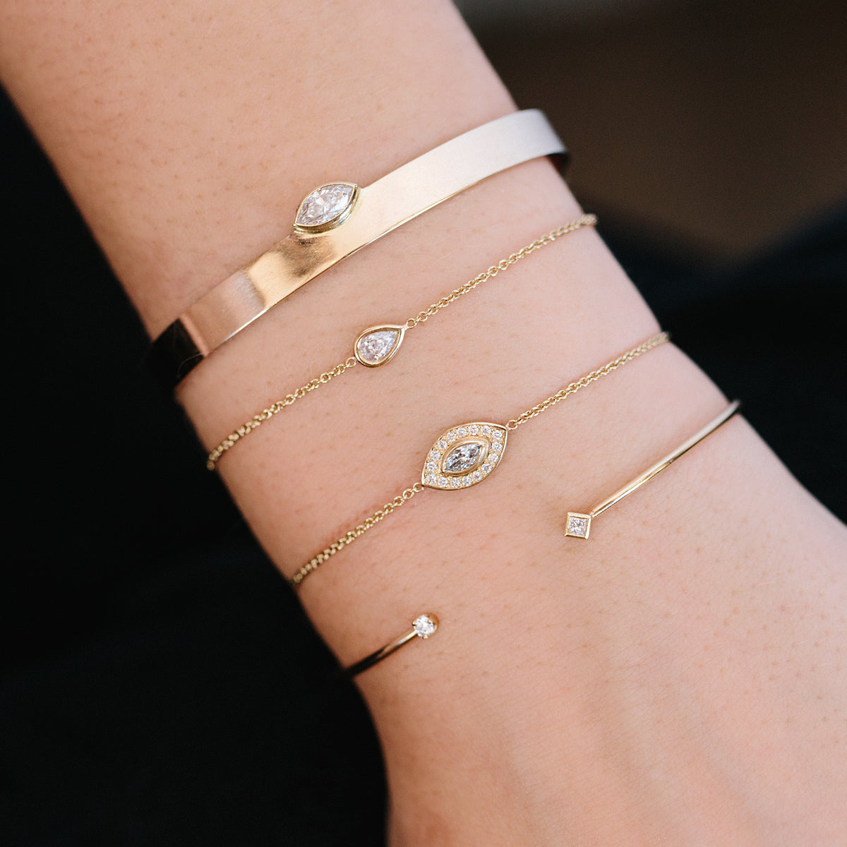 woman's wrist wearing Zoe Chicco 14kt Gold Floating Pear Diamond Bolo Bracelet stacked with two marquise diamond bracelets and a diamond cuff