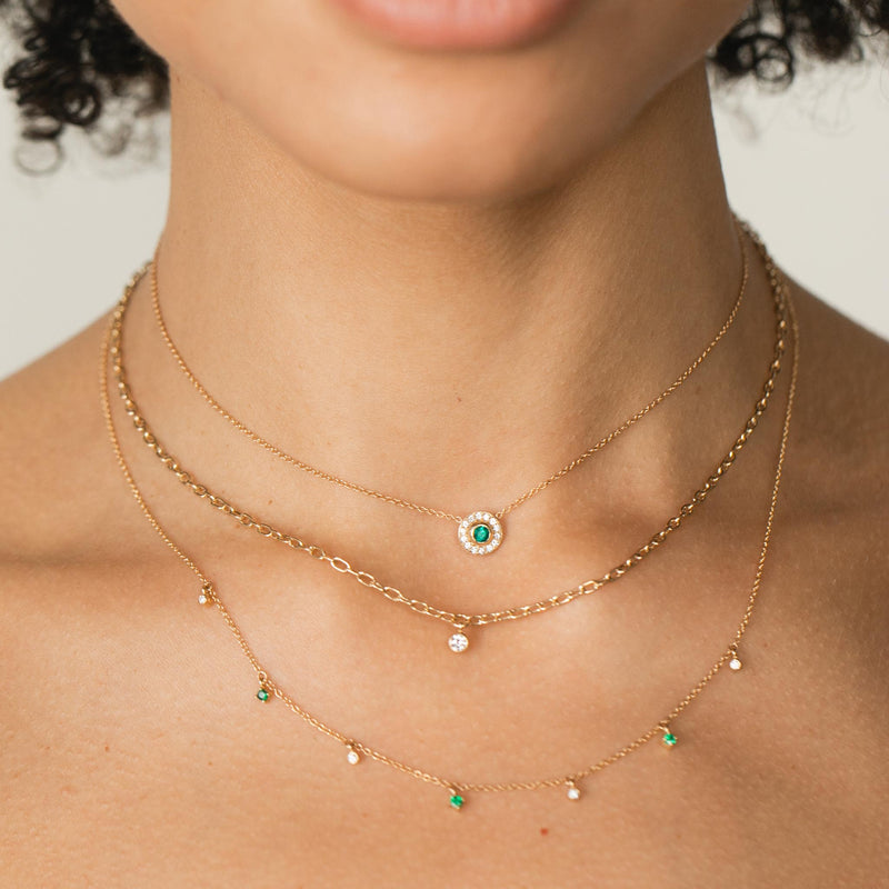 close up of woman wearing Zoë Chicco 14kt Gold Round Emerald and Diamond Halo Necklace around her neck layered with a Floating Diamond Small Square Oval Chain Necklace and a Dangling Emerald and Diamond Necklace