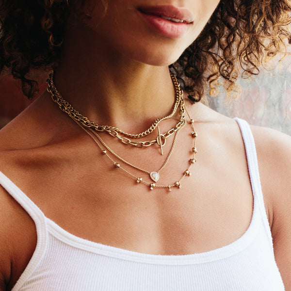 woman in a white tank top wearing a Zoë Chicco 14k Gold Pear Diamond Halo XS Curb Chain Necklace layered with a medium curb chain necklace and two other necklaces