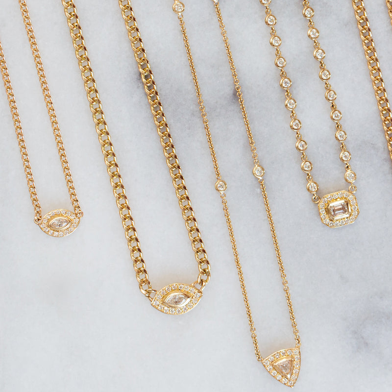 a flat lay image of Zoë Chicco 14k Gold Marquise Diamond Halo Curb Chain Necklace against a marble background