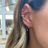 woman's ear wearing Zoë Chicco 14kt Gold Diamond Bezel Thin Huggie Hoop Earring with three other diamond bezel earrings