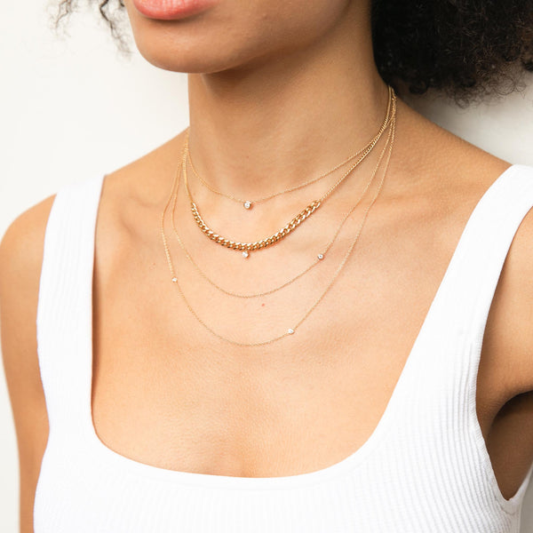 woman in white tank top wearing a Zoe Chicco 14k Gold Single Floating Diamond Necklace layered with a Mixed XS & Medium Curb Chain Station Necklace with Dangling Prong Diamond and Floating Diamond Layered Chain Necklace