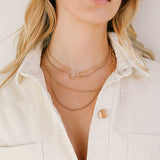 woman in a white denim button up shirt wearing a Zoë Chicco 14k Gold Pavé Diamond Safety Pin Small Curb Chain Necklace layered with two heavy chain necklaces