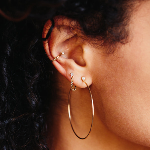close up of woman's ear wearing a Zoë Chicco 14k Gold Large Prong Diamond Hoop Earring layered with two other diamond earrings