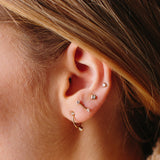 close up of woman wearing Zoë Chicco 14kt Gold Prong Diamond Barbell Stud Earrings and other diamond earrings on one ear