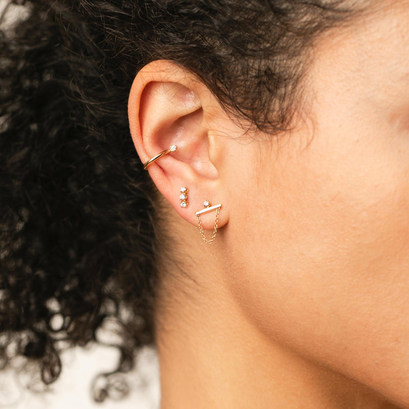 close up of woman's ear wearing a Zoe Chicco 14k Gold Prong Diamond Thick Ear Cuff layered with a 3 Prong Diamond Stud and a Prong Diamond Straight Bar Chain Stud Earring