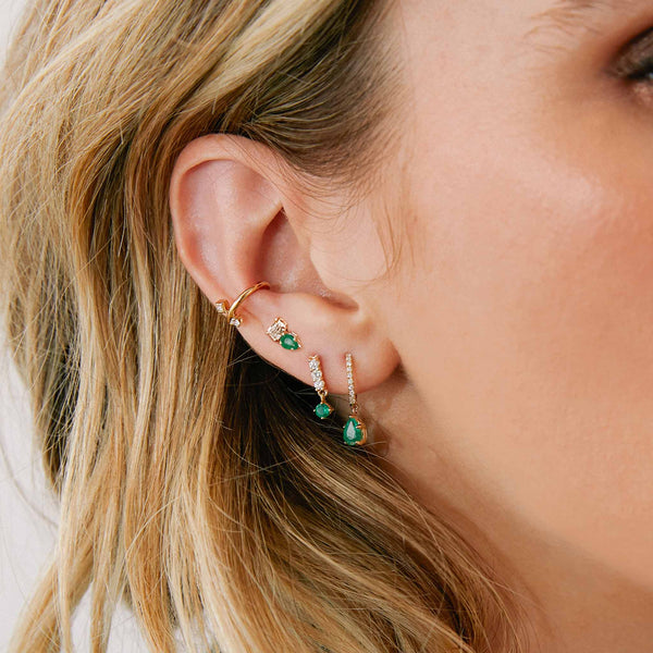 close up of a woman's ear wearing a Zoë Chicco 14k Gold Pear Emerald & Emerald Cut Diamond Stud Earring in her third piercing layered with other emerald and diamond earrings