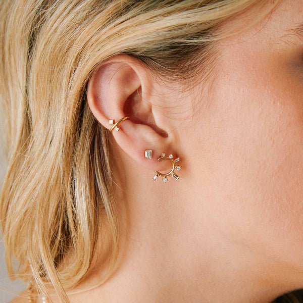 close up of a woman's ear wearing a Zoë Chicco 14k Gold Baguette & Prong Diamond Front to Back Circle Hoop Earring layered with an Emerald Cut Diamond Stud and an ear cuff
