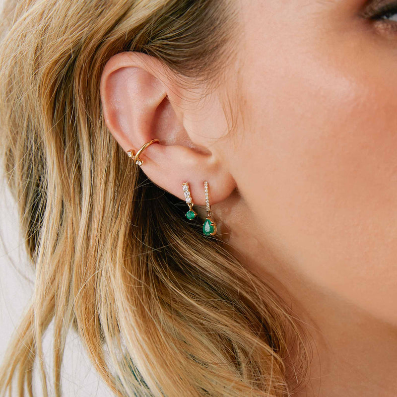 close up of woman's ear wearing a Zoë Chicco 14k Gold Diamond Bar Drop with Dangling Prong Emerald Earring layered with a Small Pavé Diamond Hinge Huggie Hoop with Pear Emerald