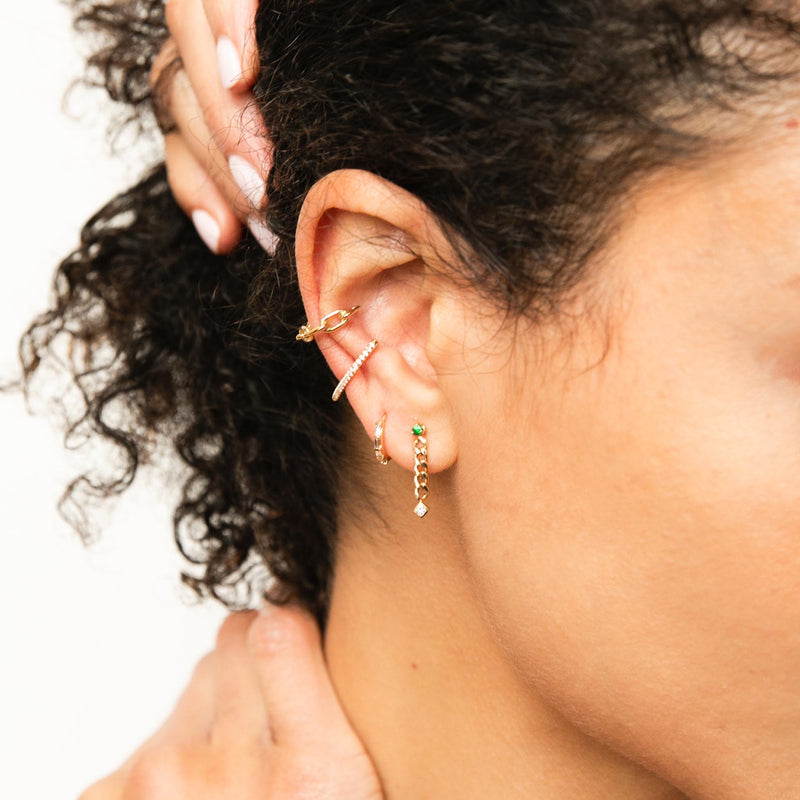 woman holding her neck and head wearing Zoë Chicco 14k Gold Pavé Diamond Thick Wire Bar Ear Cuff with a Square Oval Link Cuff layered with a Baguette Diamond Hinge Huggie Hoop and a Emerald and Princess Diamond Curb Chain Drop Earring