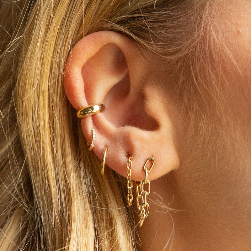 woman's ear wearing a Zoë Chicco 14k Gold Chubby Ear Cuff layered with other chain huggie and huggie hoop earrings