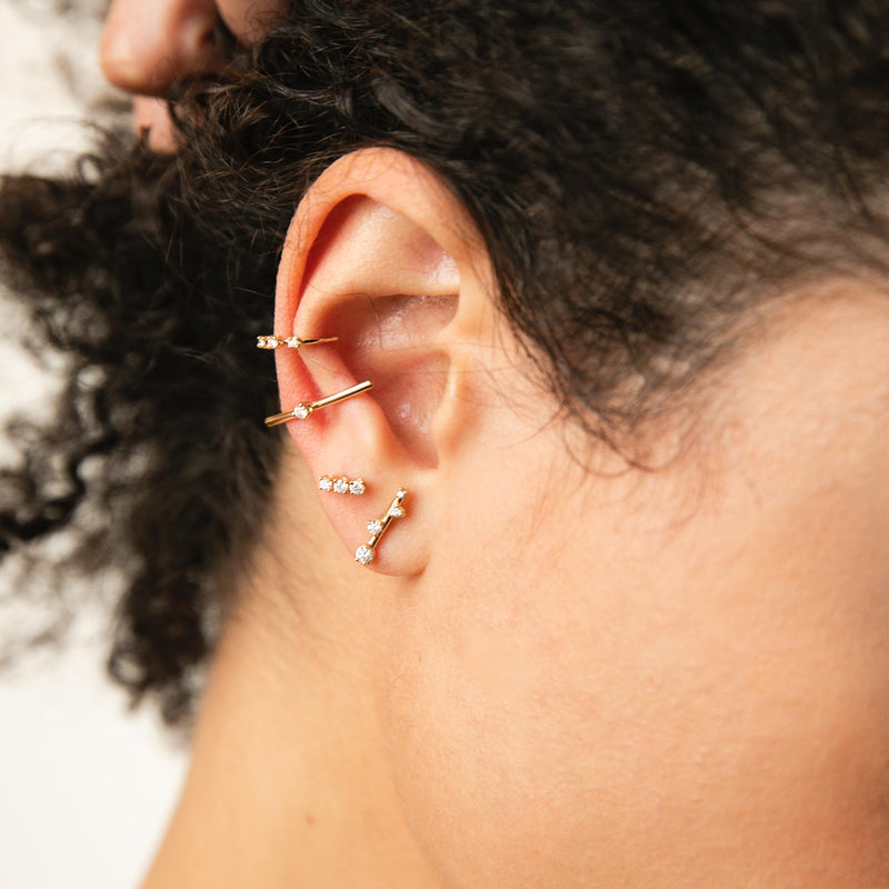 woman's ear wearing a Zoë Chicco 14k Gold Prong Diamond Thick Wire Bar Ear Cuff and Graduated Prong Set Diamond Ear cuff layered with a 3 Prong Diamond Stud and a Scattered Prong Diamond Bar Earring