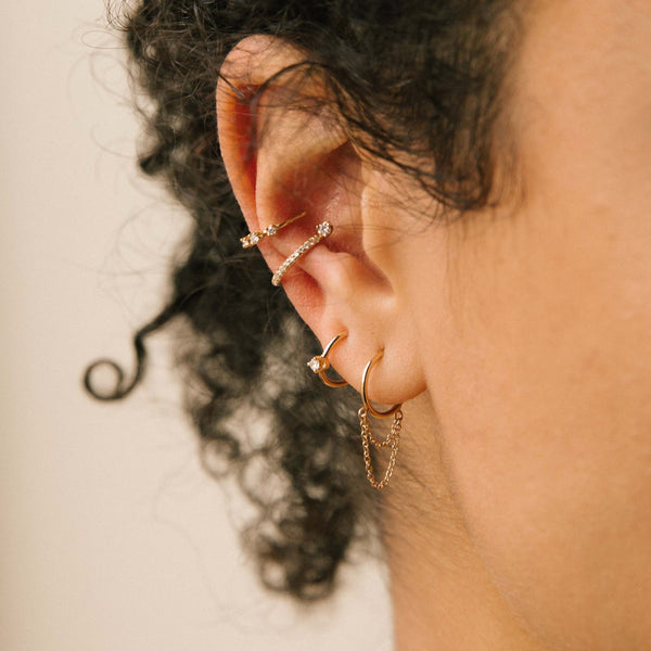 close up of woman's ear wearing a Zoe Chicco 14k Gold Graduated Prong Diamond Ear Cuff and Prong Diamond Pave Diamond Thick Ear Cuff layered with a Prong Diamond thin Huggie Hoop and a Double Chain Loop Thin Huggie Hoop