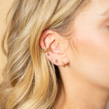 woman's ear wearing a Zoë Chicco 14k Gold Tiny Huggie Hoop Earring layered with a smiley face stud other earrings