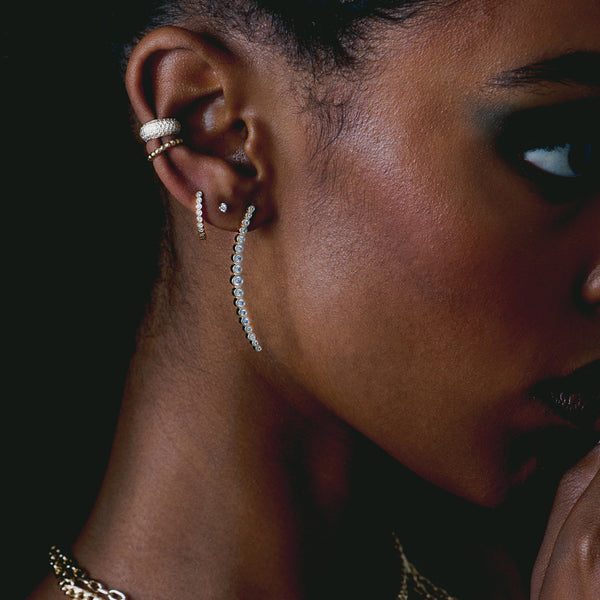 woman's side profile on a dark background wearing Zoë Chicco 14k Gold Long Graduated Diamond Curved Bar Drop Earring in her ear with several other diamond earrings