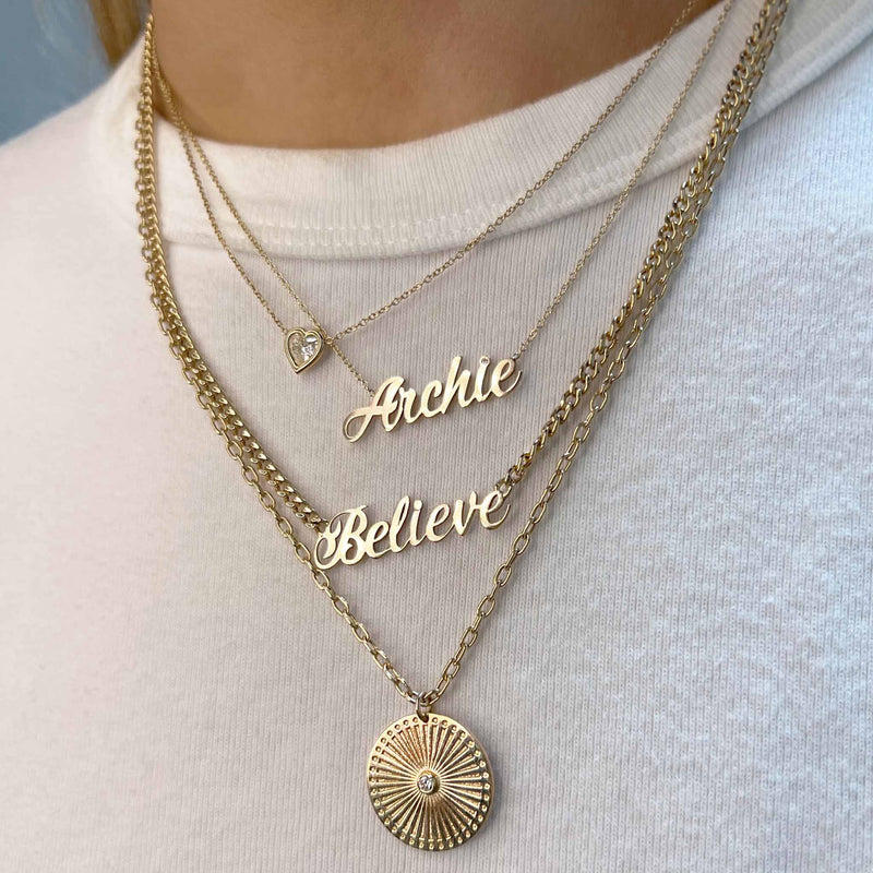 woman in white t-shirt wearing a Zoë Chicco 14k Gold Script Letter "Believe" Small Curb Chain Necklace and Custom "Archie" Script Letter Necklace with Diamond and a Floating Heart Diamond Bezel Necklace and Sunbeam Medallion Square Oval Chain Necklace