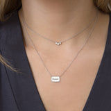 woman in dark navy top wearing a Zoe Chicco 14k White Gold Rectangle with Diamond Border Nameplate Necklace engraved with bennni