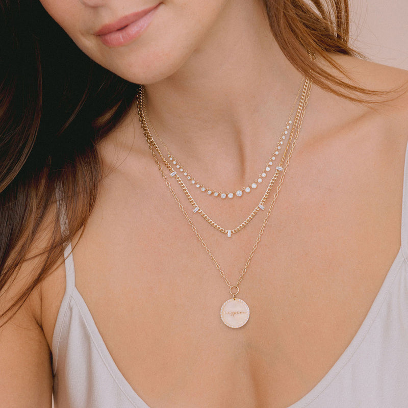 woman in camisole wearing Zoë Chicco 14k Gold Small Curb Chain Necklace with 5 Vertical Baguette Diamond Stations layered with a Graduated Diamond Bezel Necklace and a Mantra Pendant necklace