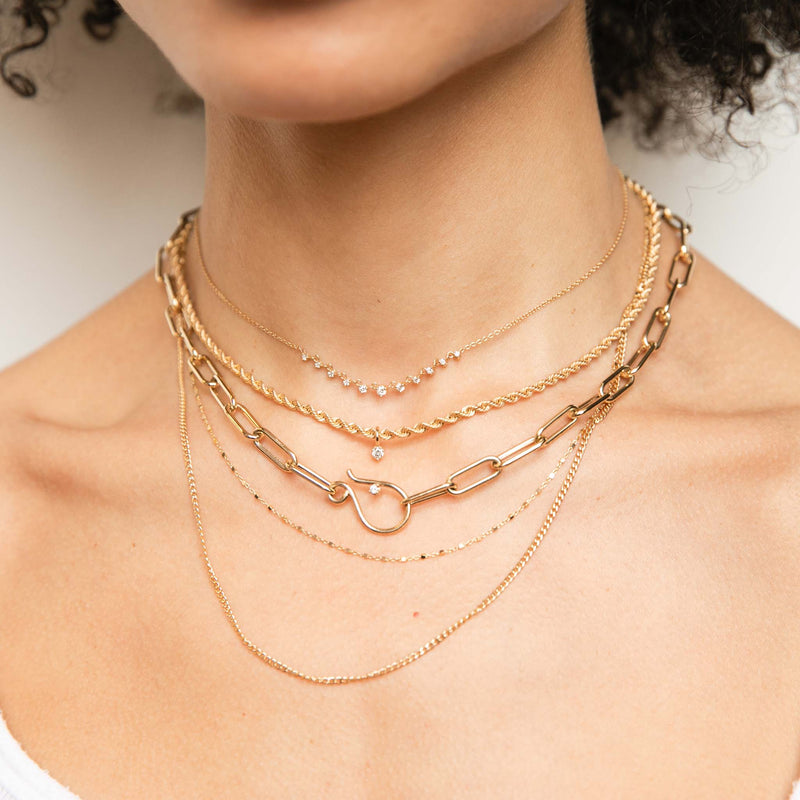 woman in white top wearing a Zoë Chicco 14k Gold 11 Linked Graduating Prong Diamond Necklace layered with a Medium Rope Chain Necklace with Dangling Prong Diamond, Large Paperclip Chain with Diamond Hook Closure, and a Square Bead & XS Curb Chain Layered Necklace
