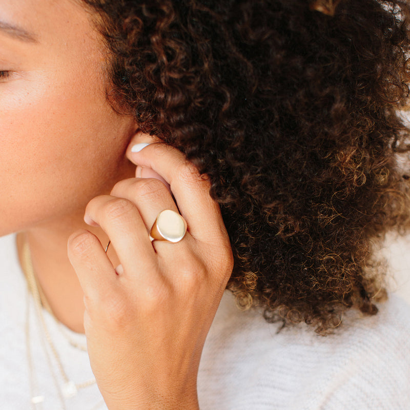 woman touching her ear and wearing Zoë Chicco 14kt Gold Large Oval Signet Ring on her middle finger