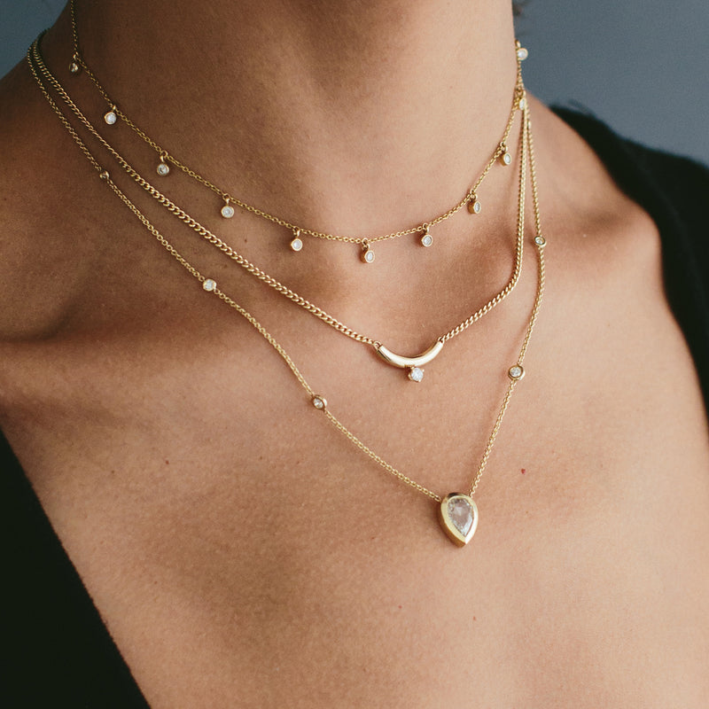 woman's neck wearing a Zoë Chicco 14k Gold Prong Diamond Chubby Bar XS Curb Chain Necklace layered with two diamond necklaces