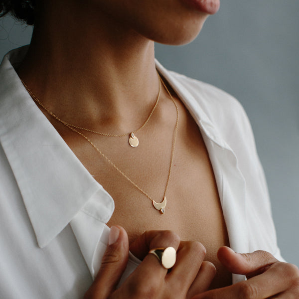 woman wearing Zoë Chicco 14kt Gold Marquise Diamond Horizon Disc Necklace, Pear Diamond Horizon Crescent Necklace, and a Large Oval Signet Ring