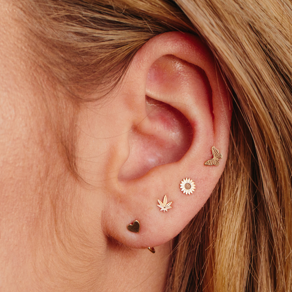 woman's ear wearing Zoë Chicco 14kt Gold Itty Bitty Butterfly, Flower, Mary Jane stud earrings with an Itty Bitty Heart Open Hoop earring