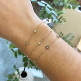 woman's wrist wearing a Zoë Chicco 14k Gold 3 Itty Bitty Diamond Flowers Bracelet layered with two other bracelets