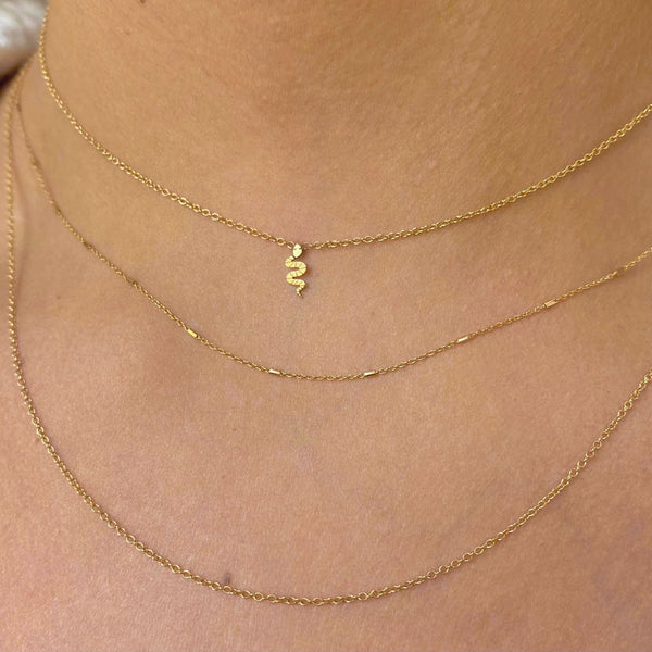 woman wearing Zoe Chicco 14k Gold Itty Bitty Snake Necklace layered with a Tiny Bar and Cable & Cable Chain Layered Necklace