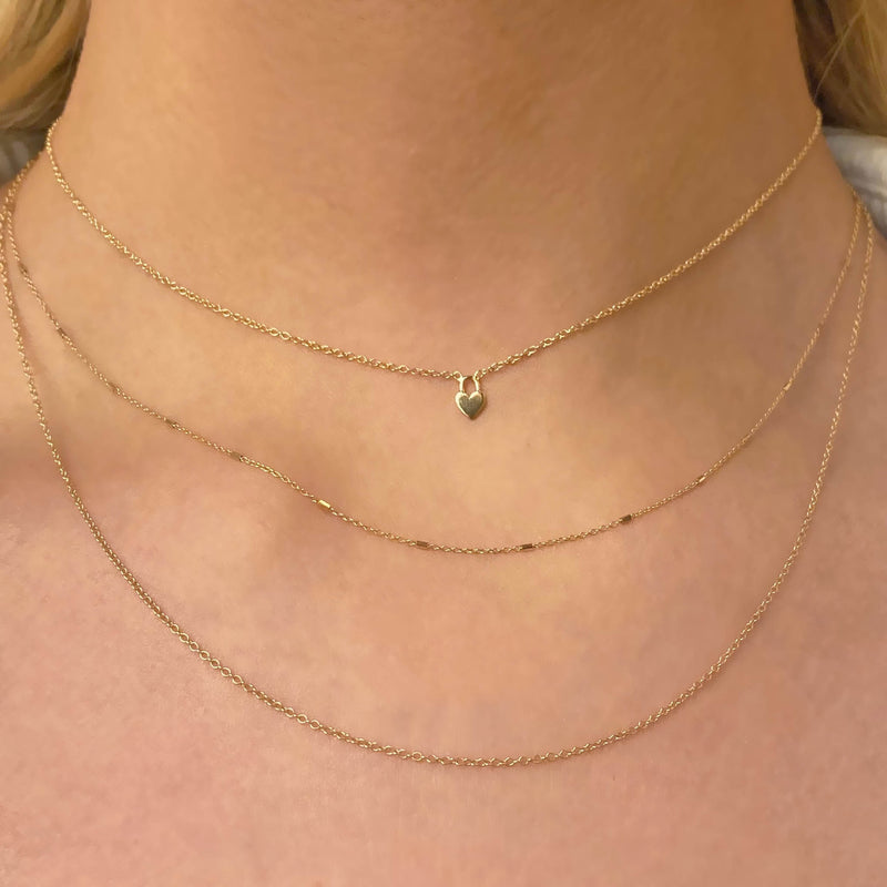 woman wearing Zoe Chicco 14k Gold Itty Bitty Heart Padlock Necklace layered with a Bar and Cable & Cable Chain Layered Necklace