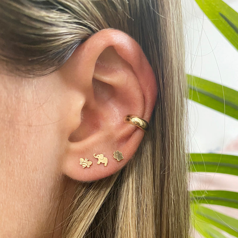 woman's ear wearing Zoë Chicco 14kt Gold Itty Bitty Elephant Stud Earring layered with an itty bitty bee and dog paw stud and a gold ear cuff