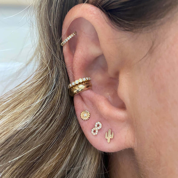 woman's ear wearing Zoë Chicco 14kt Gold Diamond Itty Bitty Flower Stud Earring with a Diamond Infinity Stud and an Itty Bitty Cactus Stud with gold and diamond ear cuffs