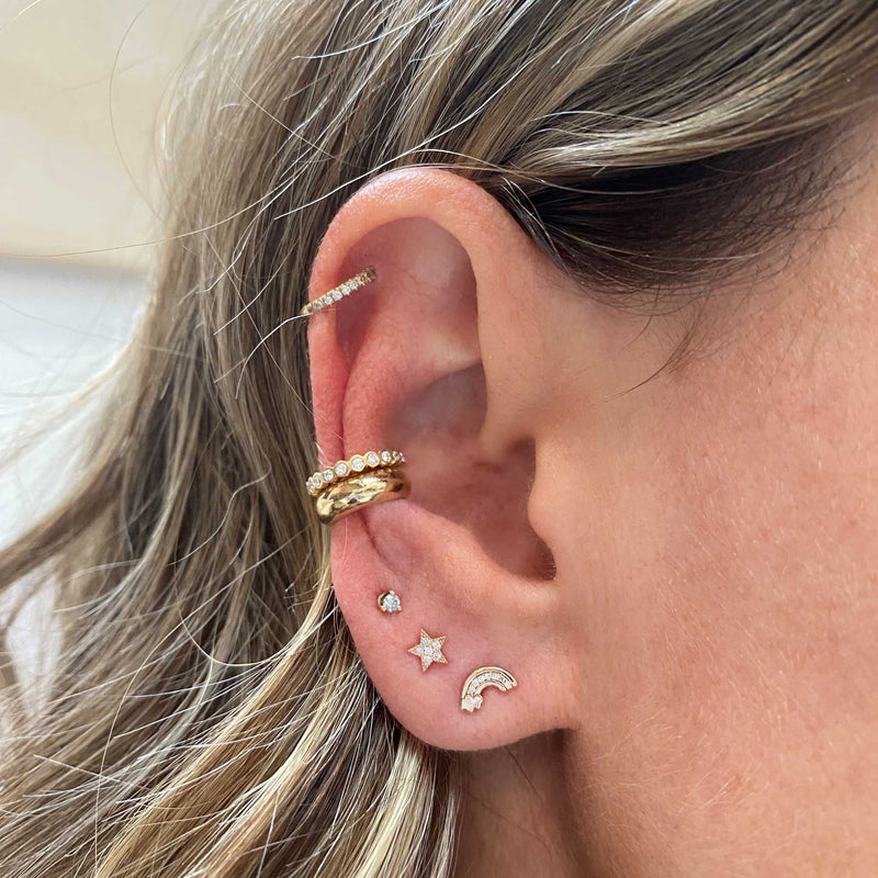 woman's ear wearing Zoë Chicco 14k Gold Itty Bitty Diamond Rainbow Stud Earring with a Pave Diamond Star Stud, Prong Diamond Stud, and diamond and gold ear cuffs