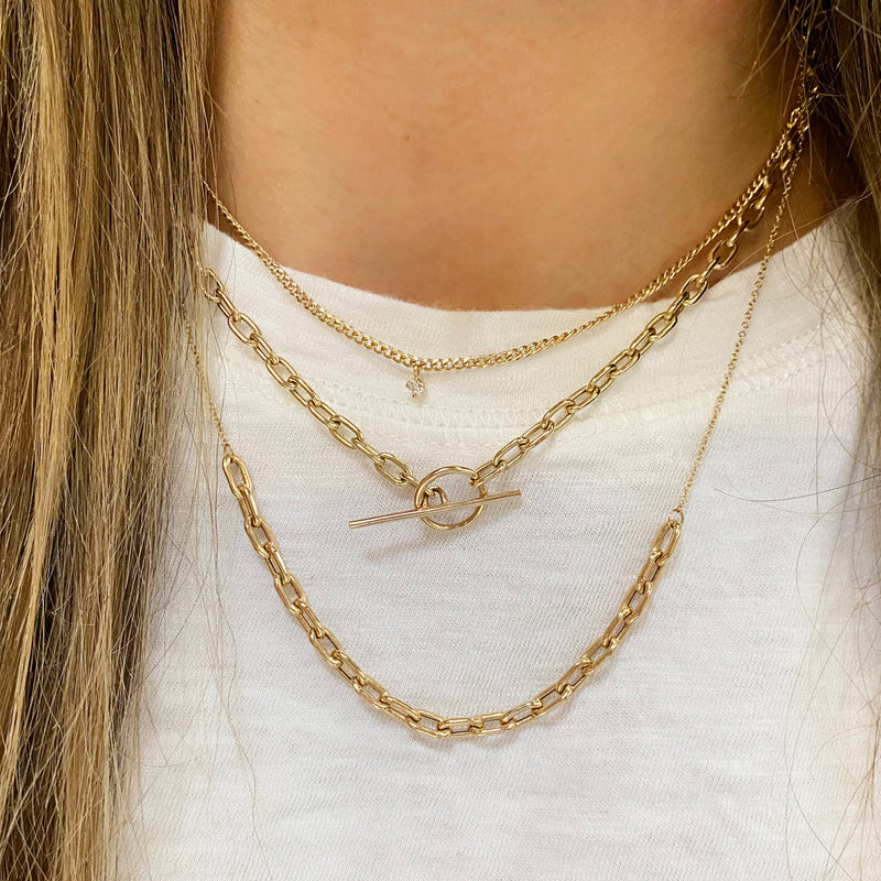 woman in white t-shirt wearing a Zoë Chicco 14k Gold Square Oval Link Station Necklace layered with two other heavy chain necklaces