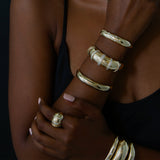 close up of woman in black camisole with one arm crossed over chest wearing Zoë Chicco 14k Gold Medium Aura Cuff Bracelet on her wrist stacked with other Aura bracelets