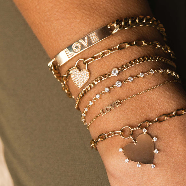 close up of woman's wrist wearing Zoe Chicco 14kt Gold Pavé Diamond Heart Padlock Bracelet  stacked with other diamond bracelets