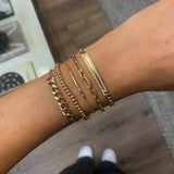 woman's wrist wearing Zoë Chicco 14k Gold Pavé Diamond Border Medium Curb Chain ID Bracelet stacked with a small gold bead bracelet and other heavy chain bracelets