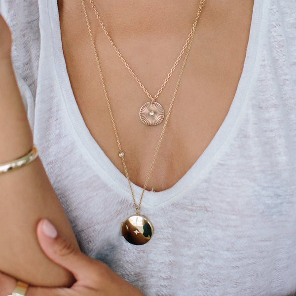 woman in a white v neck tshirt wearing a Zoë Chicco 14k Gold Star Set Diamond Round Locket Necklace with Floating Diamond layered with a sunbeam medallion necklace