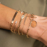 close up of woman's wrist wearing Zoë Chicco 14k Gold Large Square Oval Link "BE THE CHANGE" ID Bracelet with 2 Diamonds layered with a Mixed 2 Prong Diamond Cuff, Marquise Diamond Halo Curb Chain Bracelet, Diamond Bezel Bar Bracelet, and Mantra Charm Square Oval Link Chain Toggle Bracelet