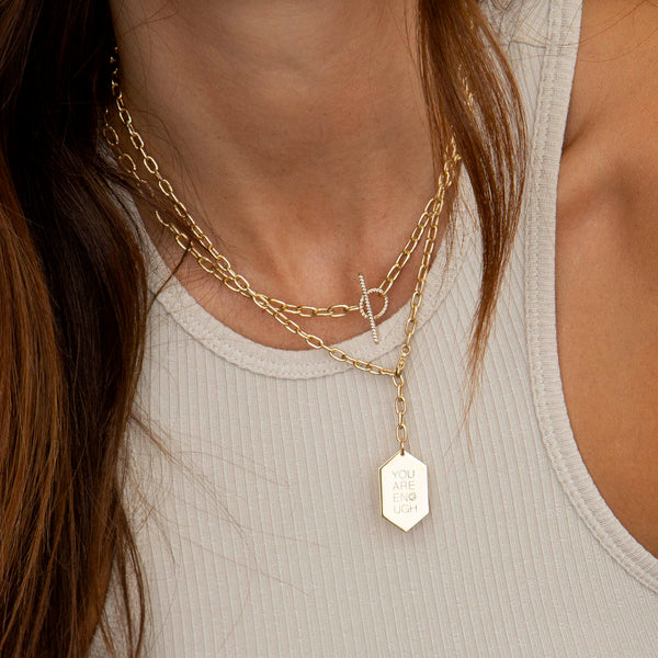 woman in beige tank top wearing Zoë Chicco 14k Gold Large Square Oval Link Pavé Diamond Toggle Necklace layered with a You Are Enough Hexagon Tag Lariat Necklace
