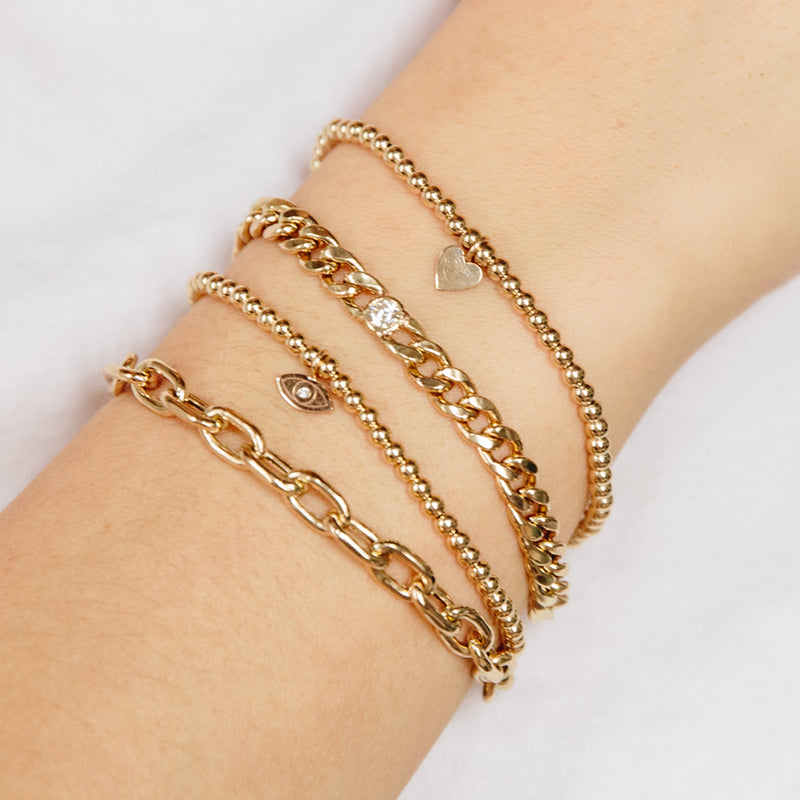 woman's wrist wearing Zoë Chicco 14k Small Gold Bead Bracelet with Diamond Evil Eye layered with three other bracelets