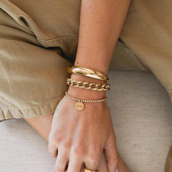 woman resting her hand on her leg wearing a Zoe Chicco 14kt Gold XXL Open Link Curb Chain Bracelet on her wrist