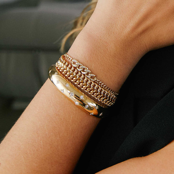 woman's wrist wearing a Zoë Chicco 14k Gold Small Curb Chain Bracelet with Pavé Diamond Large Curb Link Station layered with two other bracelets