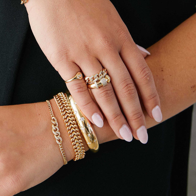 woman with her hand resting on her arm wearing a Zoë Chicco 14k Gold 3 Pavé Diamond Link Large Curb Chain Ring layered with a 14k Pavé Diamond Banded Door Knocker Half Round Ring on her ring finger