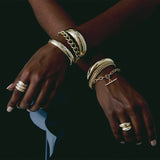woman's arms crossed on her lap on a dark background wearing Zoe Chicco 14kt gold bracelets and rings stacked together