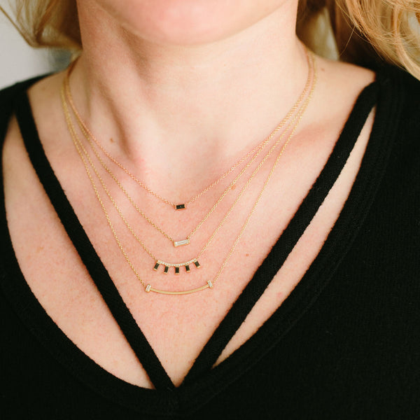woman in black top wearing Zoë Chicco 14kt Gold Vertical Baguette Diamond Curved Bar Necklace layered with a Diamond Curved Bar Black Baguette Necklace, Large Baguette Diamond Necklace, and a Black Baguette Diamond Necklace