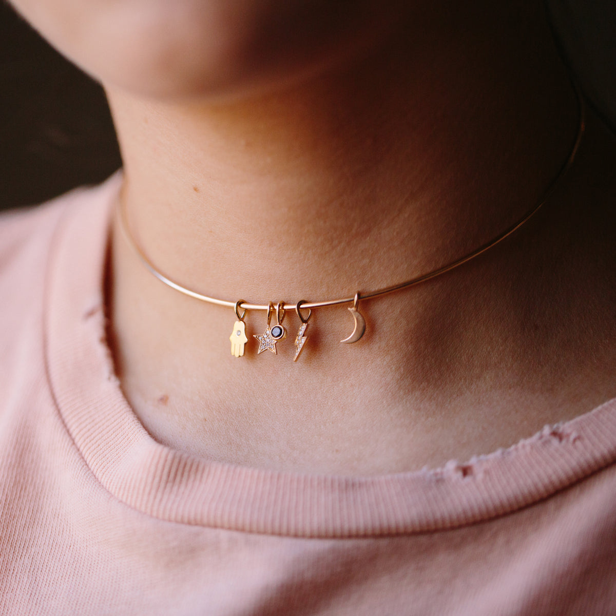 woman wearing a 14 karat gold collar necklace with a black diamond bezel charm, moon charm, hamsa with diamond charm, and pave diamond star and lightning bolt charm