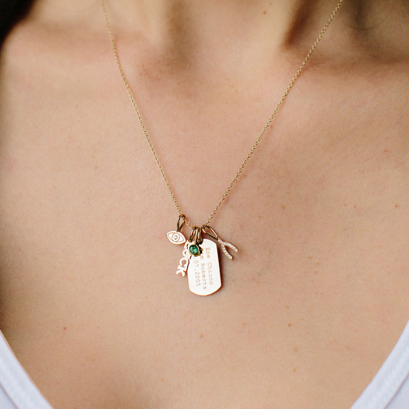 woman wearing Zoë Chicco 14kt Gold Vertical Text Small Dog Tag Charm with an Emerald Charm, Evil Eye with Diamond Charm, Pave Diamond Horseshoe charm, and Itty Bitty Luck Charm