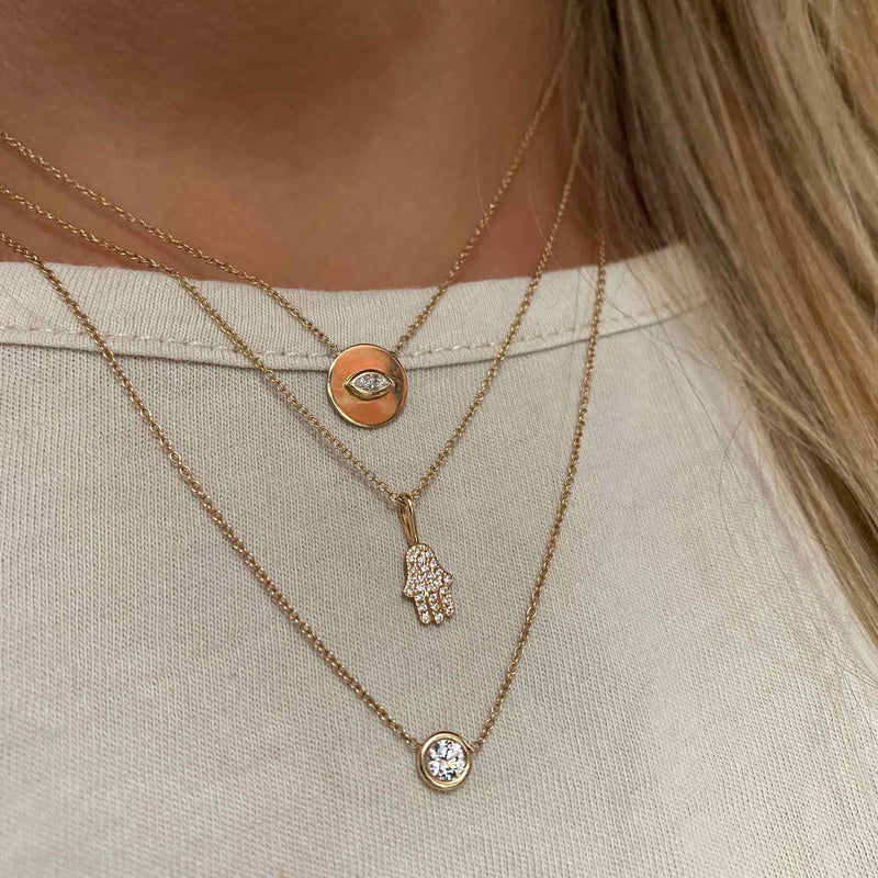 close up of woman in white t-shirt wearing 14k Marquise Diamond Small Disc Pendant Necklace layered with a Pave Diamond Midi Bitty Hamsa necklace