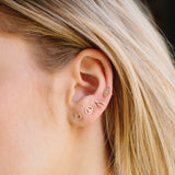 woman's ear wearing Zoe Chicco 14kt Gold Midi Bitty Wishbone Stud, Peace Sign Stud, Evil Eye with Diamond Stud, and Pave Diamond Horsehoe Stud